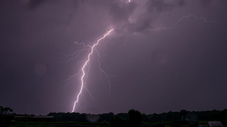 A bolt of lightning illuminates the early evening sky over...