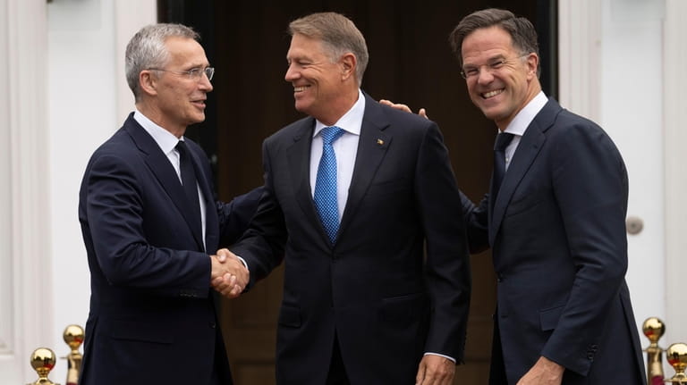 Romania's President Klaus Iohannis, center, is greeted by NATO Secretary...