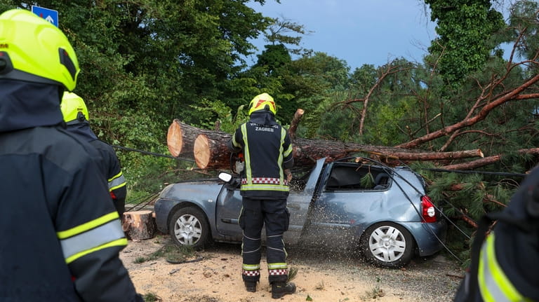 Firefighters remove fallen tree branches from damaged parked car after...
