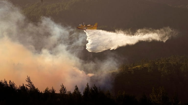 A seaplane discharges water on the flames as the fire...
