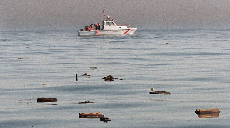 Crew members aboard a U.S. Coast Guard boat pick up pieces...