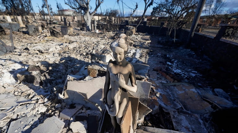 A burnt statue sits amid the rubble of a home,...