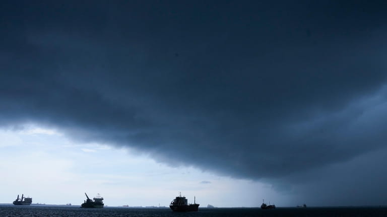 Storm clouds gather overhead as cargo ships that wait to...