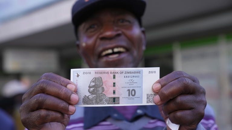 A man smiles while holding the new Zimbabwean banknote, called...