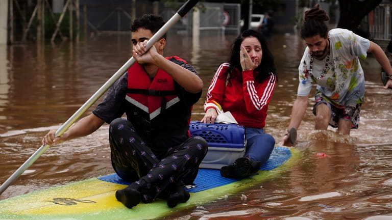 People evacuate on a surfboard from a neighborhood flooded by...
