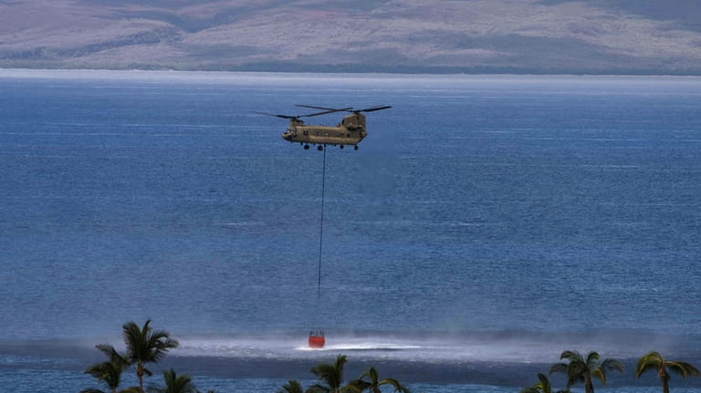 A Chinook helicopter scoops up water from the ocean near...