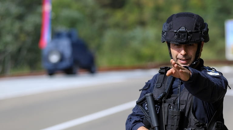 A Kosovo police officer guards a road near the village...