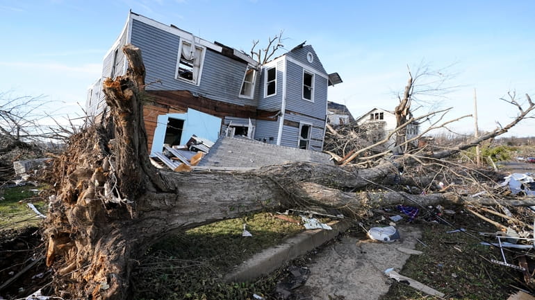 An overturned tree sits in front of a tornado damaged...