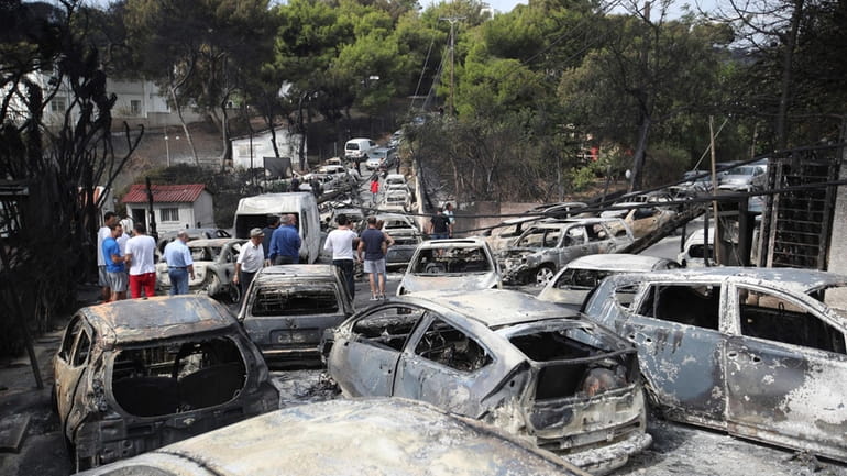 People stand amid the charred remains of burned-out cars in...