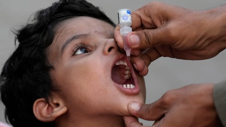 A health worker administers a polio vaccine to a child...
