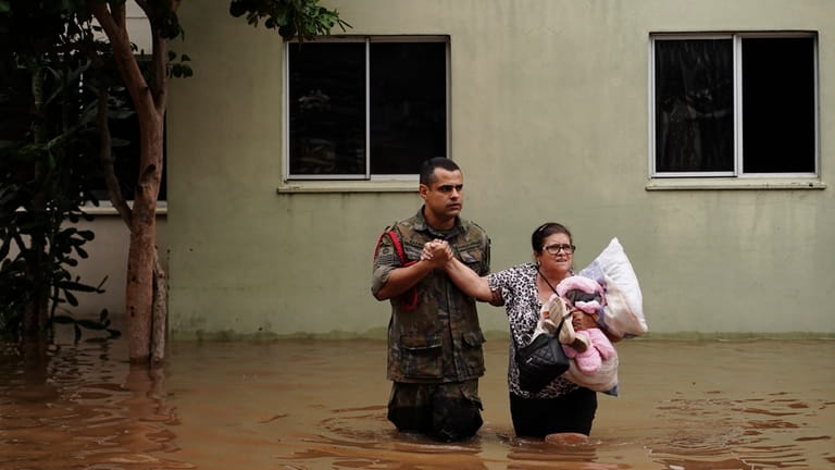 A soldier helps a woman evacuate from a neighborhood flooded...