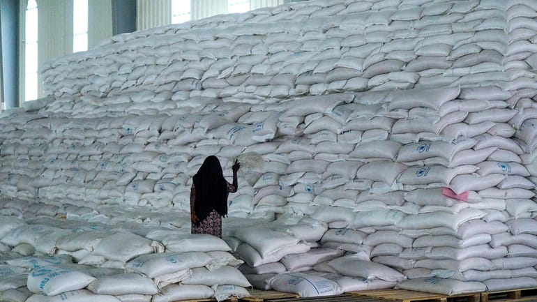 A worker walks next to a pile of sacks of...