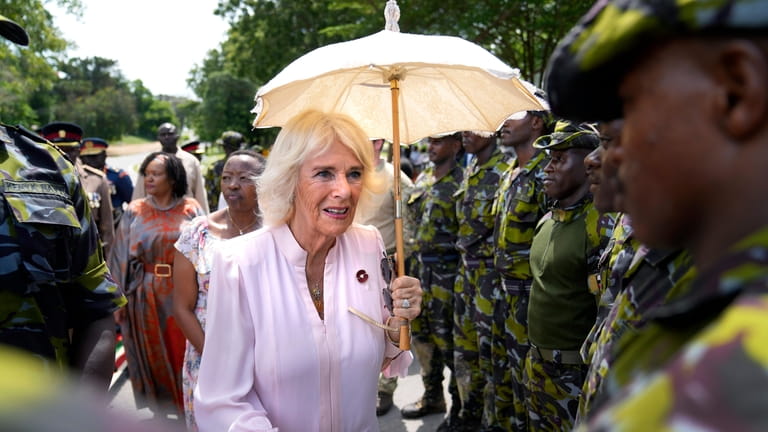 Britain's Queen Camilla holds an umbrella as she shakes hands...