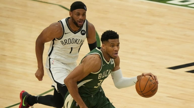The Bucks' Giannis Antetokounmpo drives past the Nets' Bruce Brown...