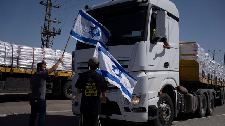 Holding Israeli flags people stand in front of trucks carrying...