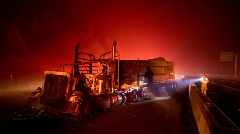 A scorched logging truck rests on Interstate 5 as the...