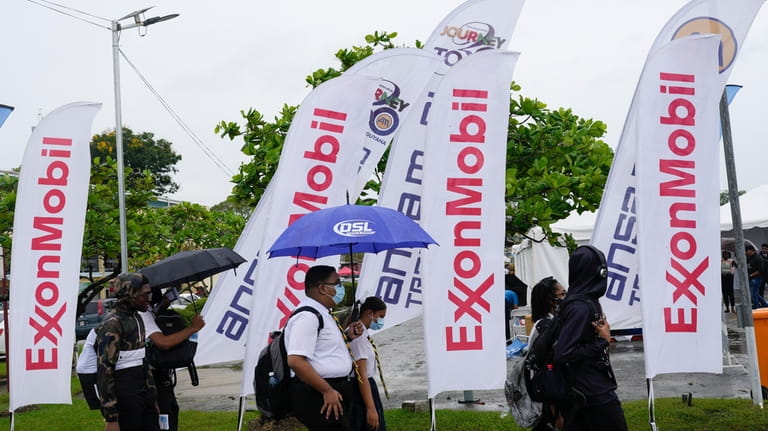 File - High school students walk past ExxonMobil flags as...