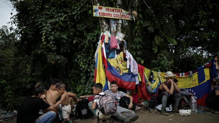 Migrants sit under a sign marking the Panama-Colombia border during...