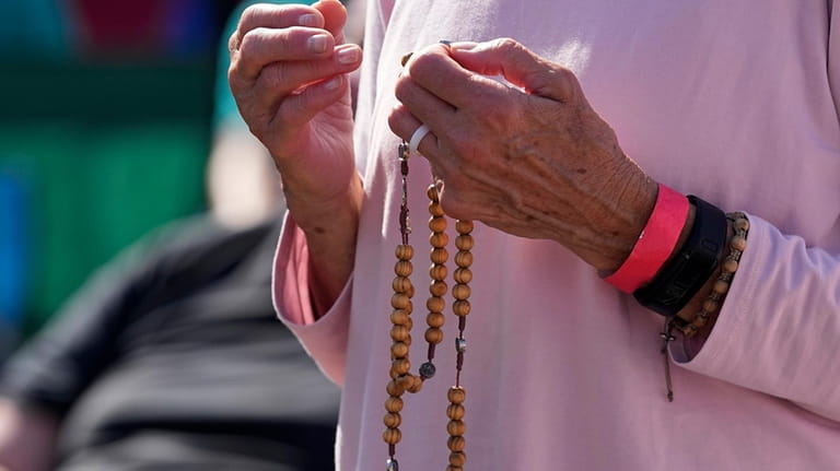 An attendee holds a rosary as she prays during a...