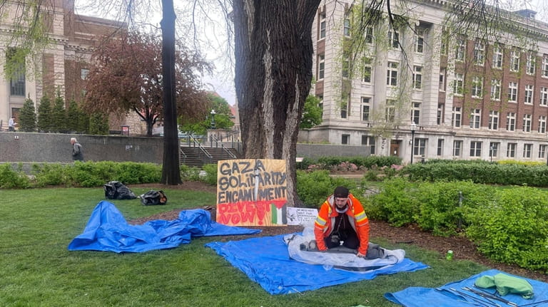 A graduate student in orange rolls up tents in front...