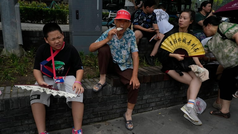 Tourists eat popsicle and fan themselves to cool off from...