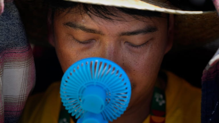 A World Youth Day volunteer uses a small fan to...