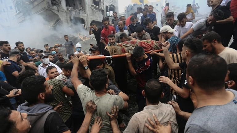 Palestinians remove a dead body from the rubble of a...