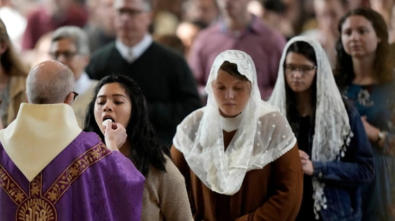 People receive communion during Catholic Mass at Benedictine College Sunday,...