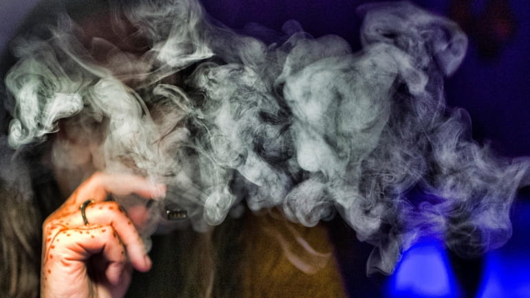 A woman takes a puff from a cannabis vape pen in...