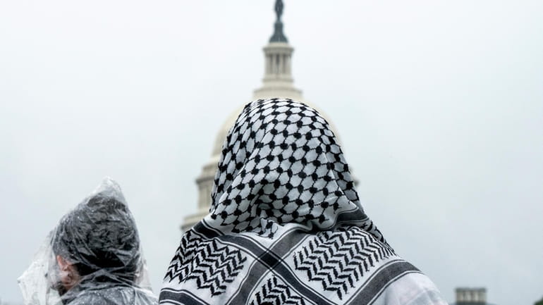 A man wearing a keffiyeh looks at the U.S. Capitol...
