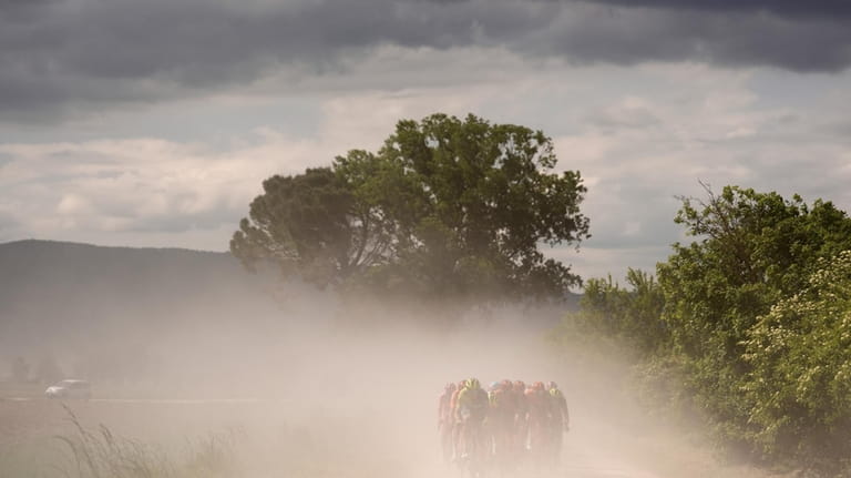 Cyclists ride through the dust along the Tuscan countryside during...