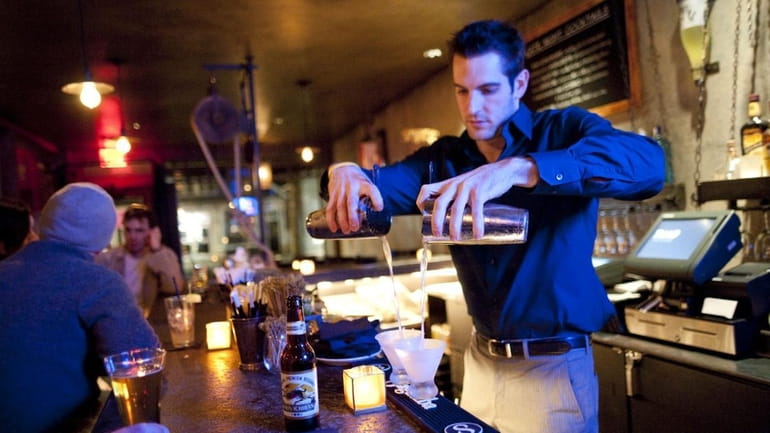 Bartender Harrison Platz mixes drinks behind the bar at Phao,...
