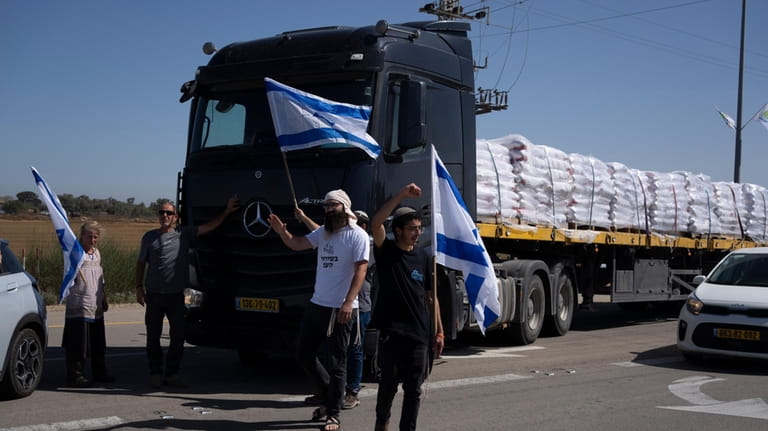 Holding Israeli flags people stand in front of trucks carrying...