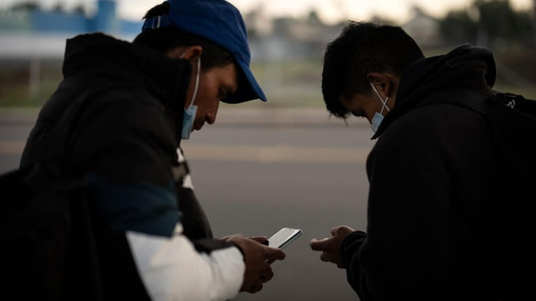 Migrants check their phones as they arrive at a bus...