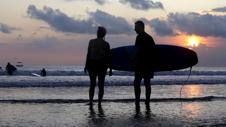 Tourists watch the ocean during sunset at Kuta beach in...