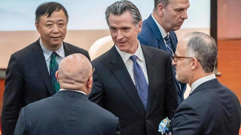 Visiting California Gov. Gavin Newsom, center, is greeted by guests...