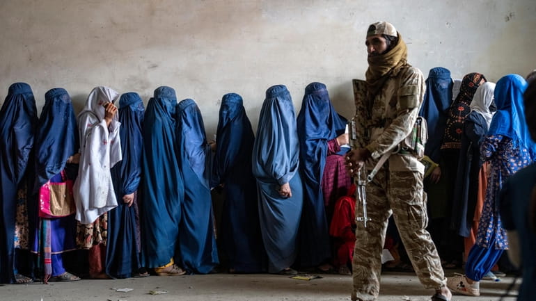 A Taliban fighter stands guard as women wait to receive...