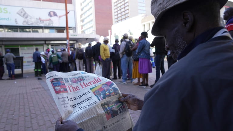 A man reads a Newspaper while waiting in a queue...