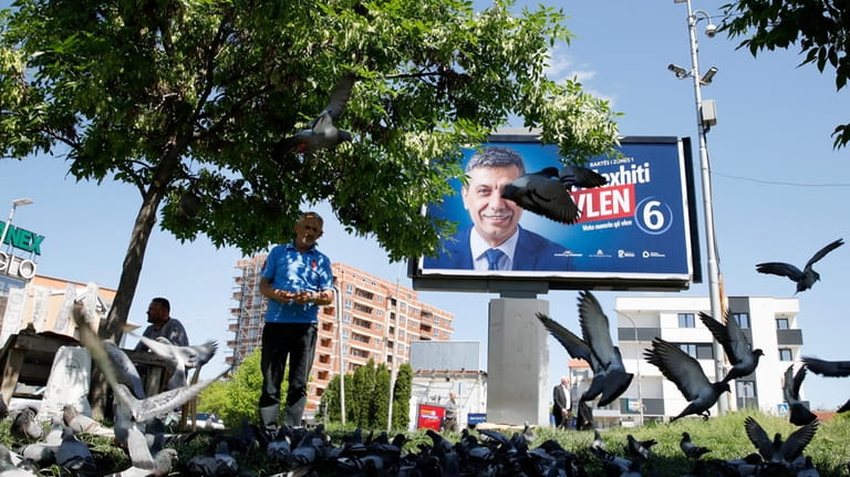 A man feeds pigeons near an electoral poster of Izet...