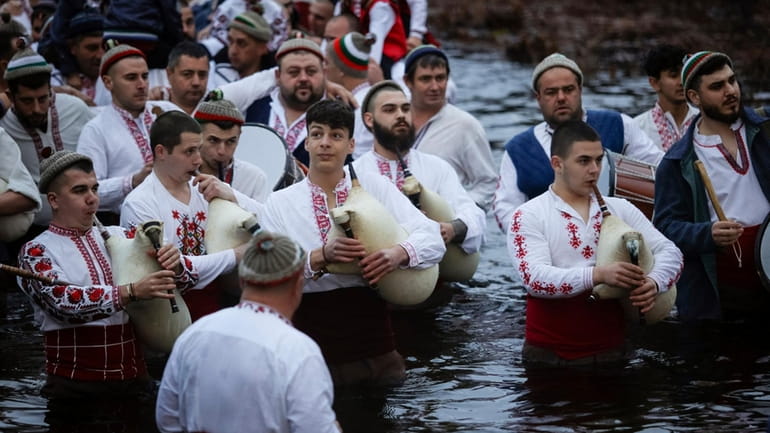 Men play bagpipes and drums as they wade into the...