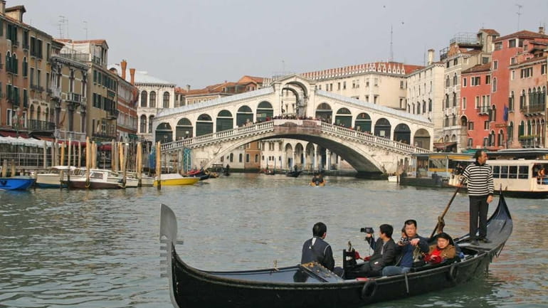 A gondolier takes passengers for a ride on the Grand...