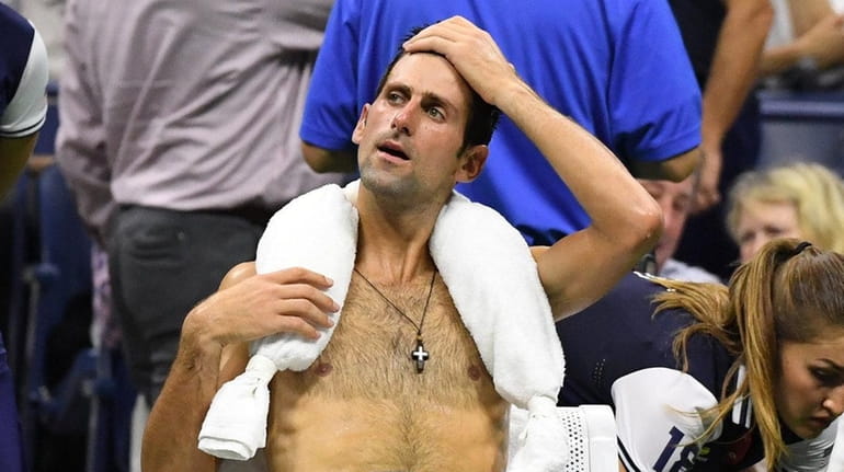 Novak Djokovic sits with an ice towel around his neck...