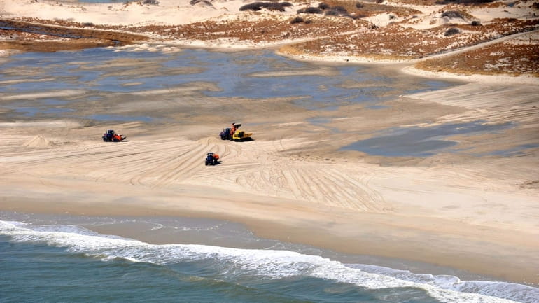 An aerial photo shows bulldozers pushing sand into pools of...