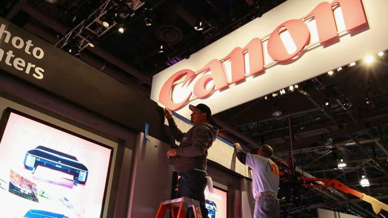 Workers apply vinyl letters at the Canon booth the day...