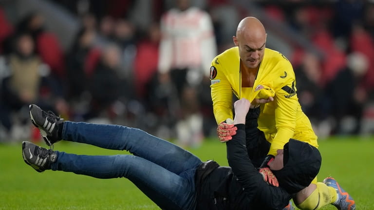 A PSV supporter, on the ground, attacks Sevilla's goalkeeper Marko...