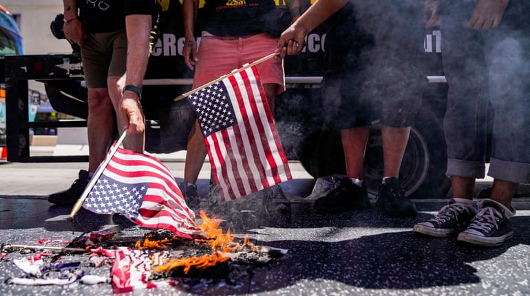 Protesters set an American flag on fire near the Hollywood...