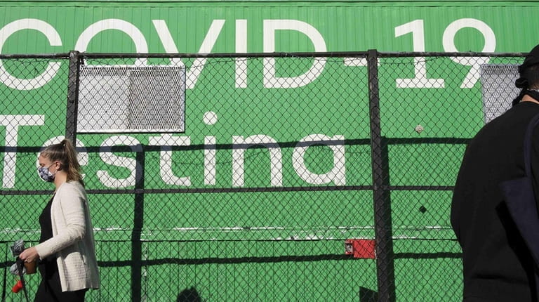 People walk past a sign for a COVID-19 testing site...