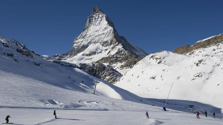 Skiers ride down the slopes at Riffelberg with Mount Matterhorn...