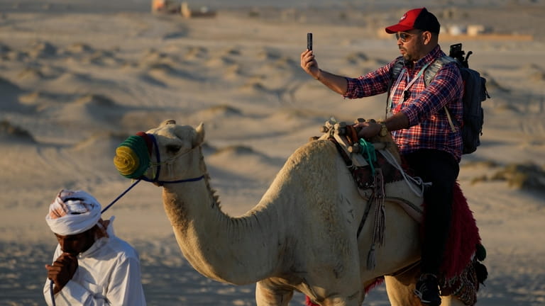 A man takes a selfie while riding camels in Mesaieed,...
