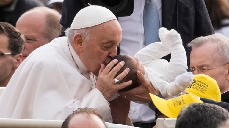 Pope Francis kisses a new born as he arrives for...